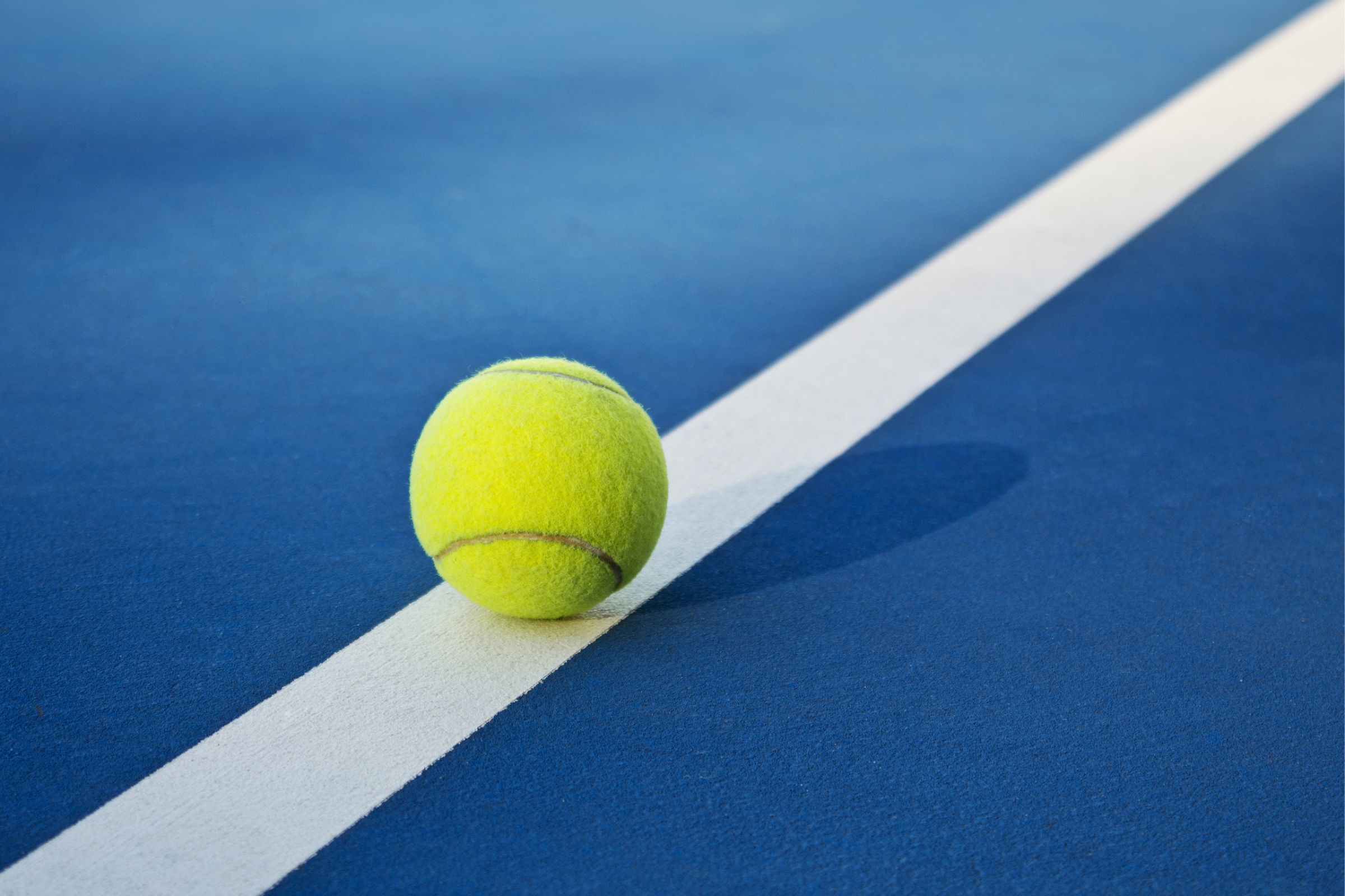 Photo of a yellow tennis ball on a blue court