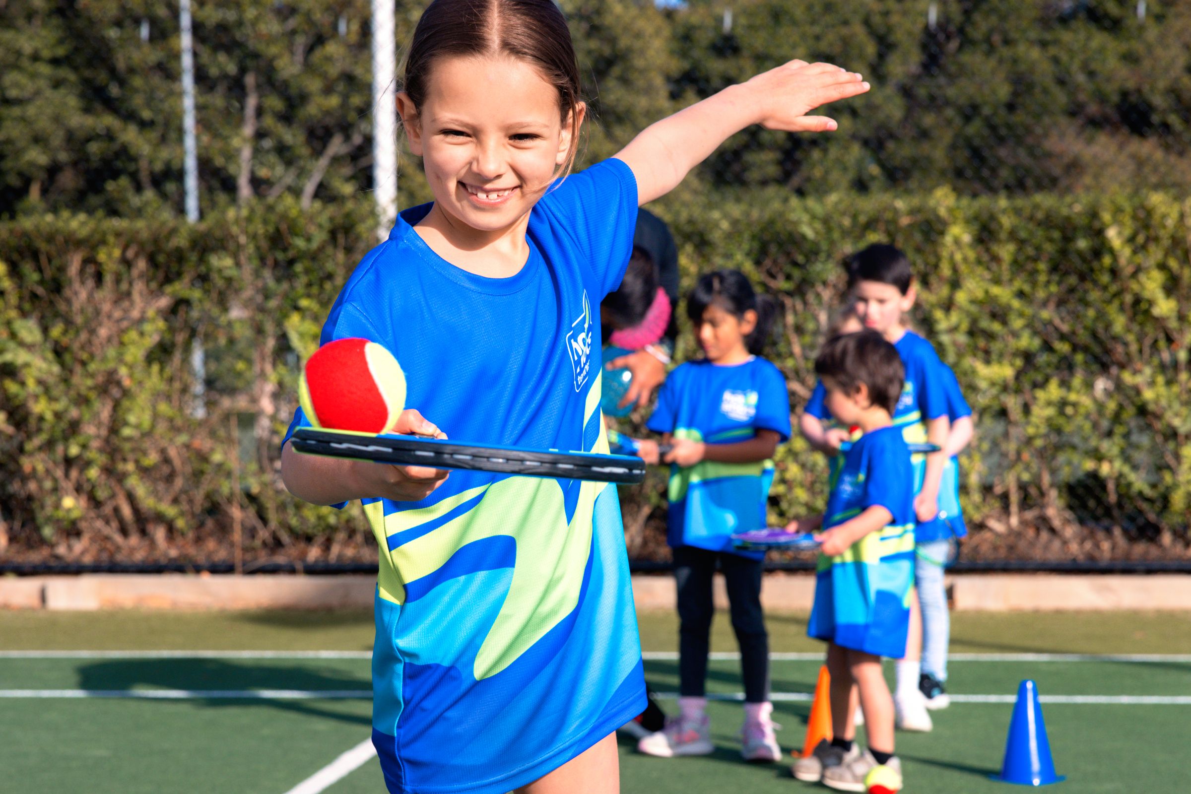 Photo of a young girl holding a tennis racquet with a red ball on it