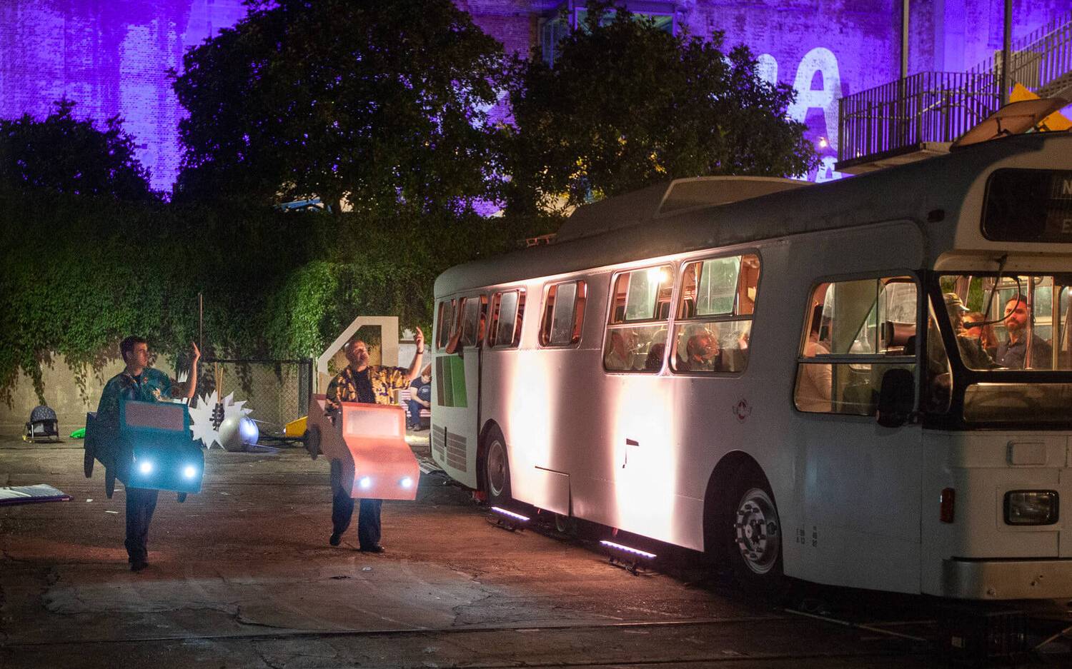 Two actors wearing car props next to a bus for the Speed: The Movie, The Play performance